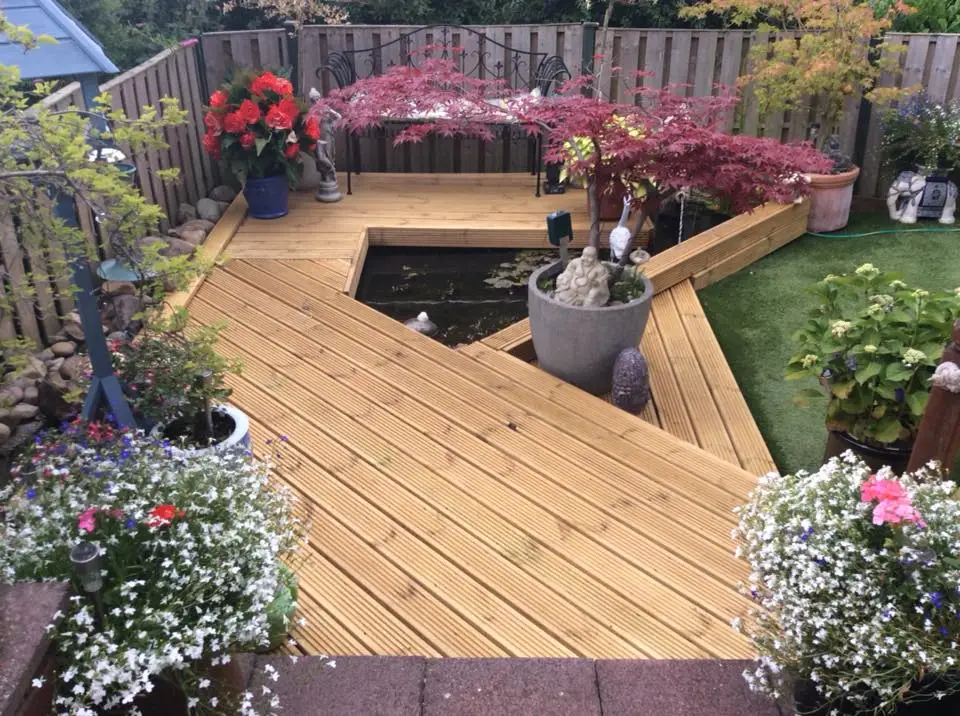 A landscaped garden featuring wooden decking in Sheffield, surrounding a small pond with decorative plants, flowers, and garden ornaments.