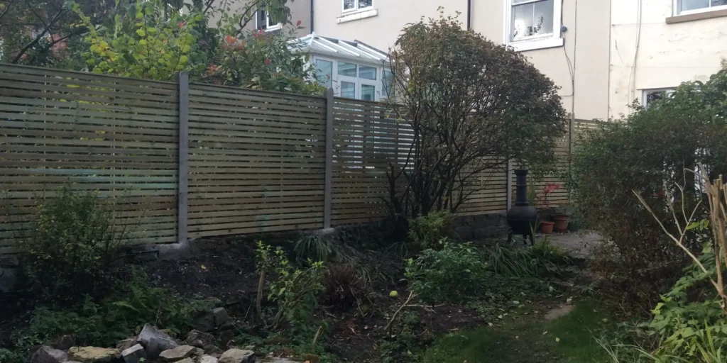 Garden area after hedge and tree removal in Sheffield, showing newly cleared space beside a wooden fence.
